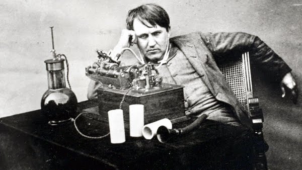 A photo of Thomas Edison, in a slouching pose behind some of his inventions. A photo of Thomas Edison, in a slouching pose behind some of his inventions.